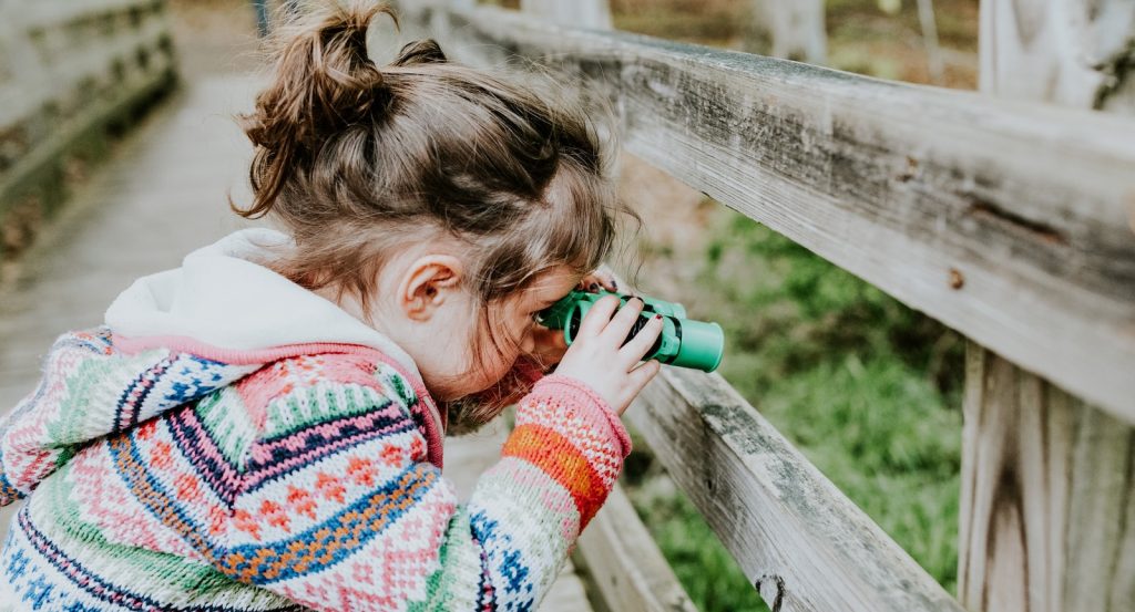 girl in white and red sweater leaning on brown wooden fence during daytime